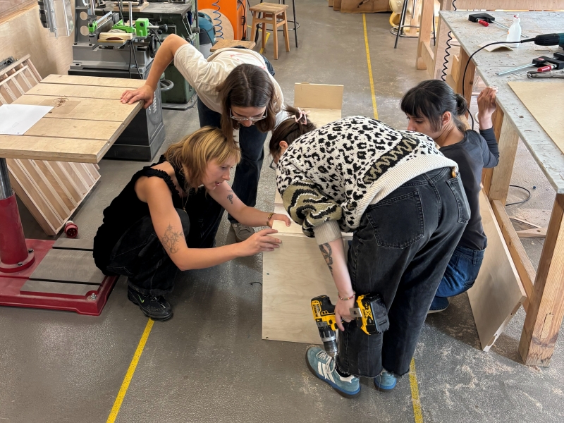 Grupa studentek School of Form pochyla się nad meblem i omawia projekt.