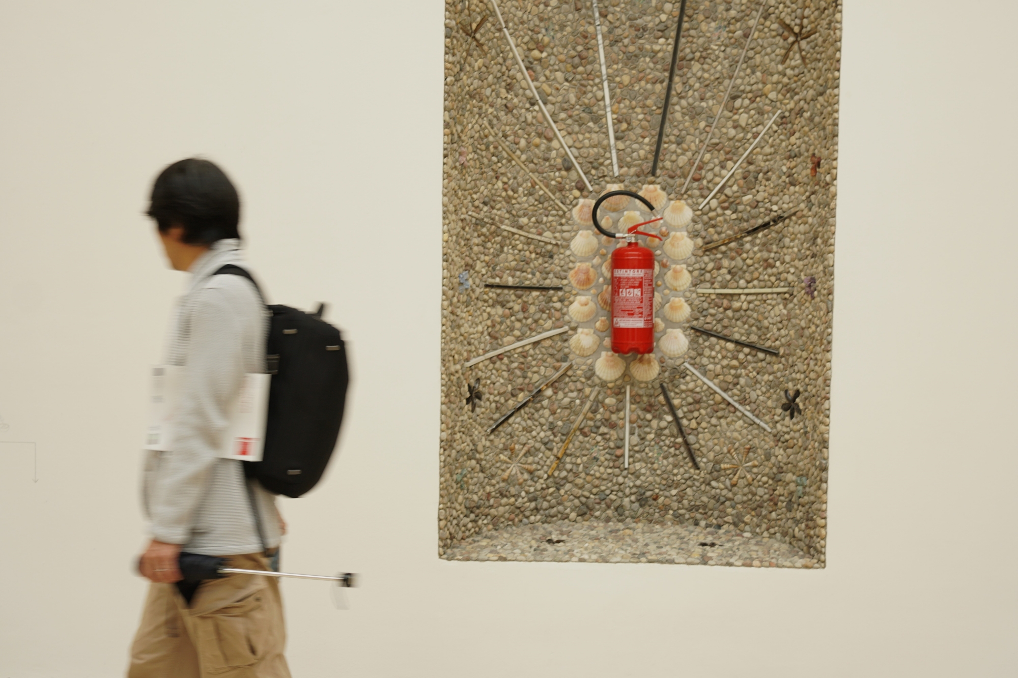 A fire extinguisher as part of the exhibition; a visitor walks by