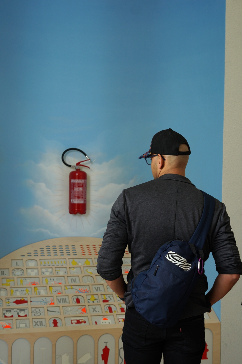 Man looking at a fire extinguisher, one of the objects featured in the “Lares and Penates” exhibition