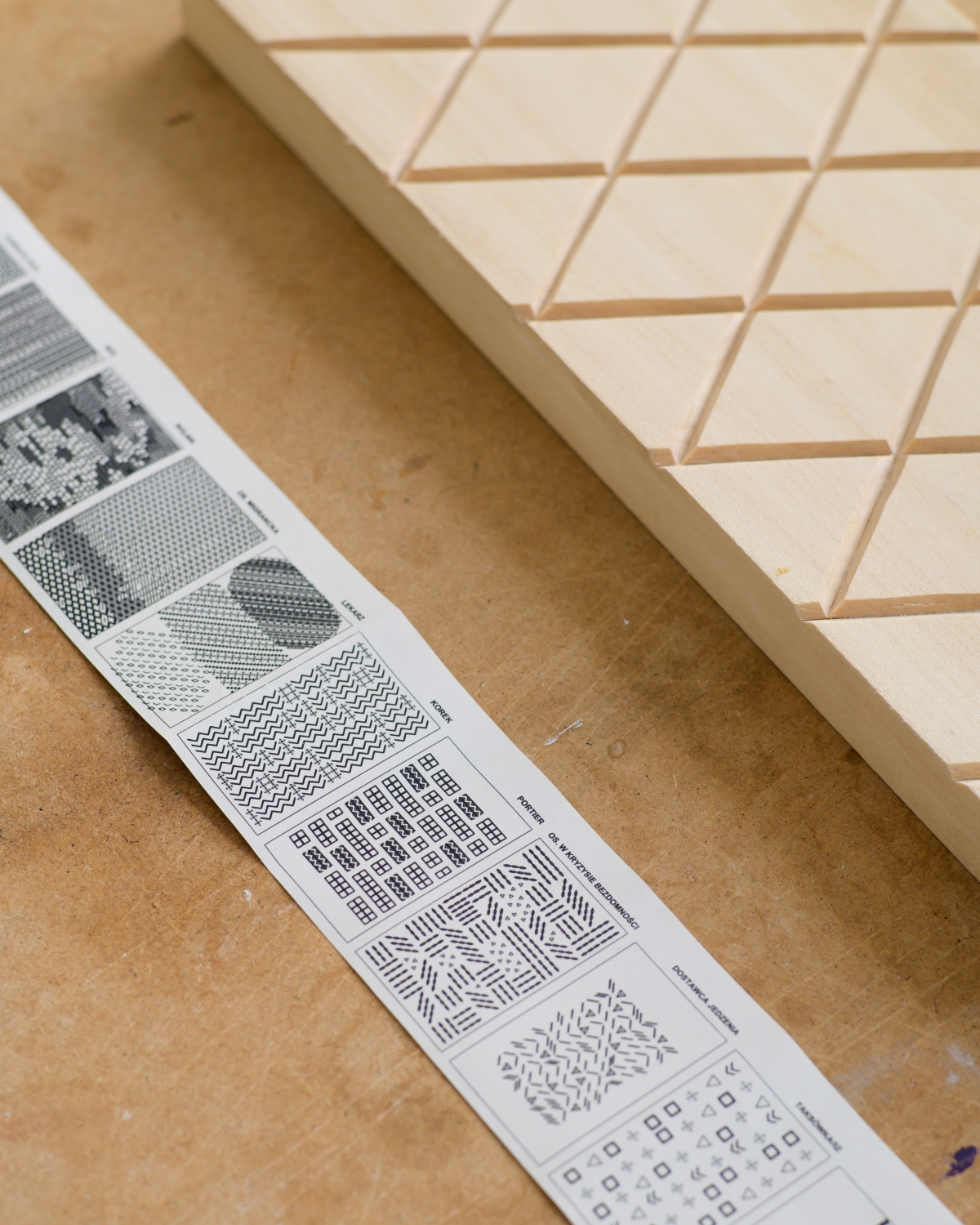 Wooden tile with a cut-out geometric pattern; next to it, a sheet with different geometric pattern drafts