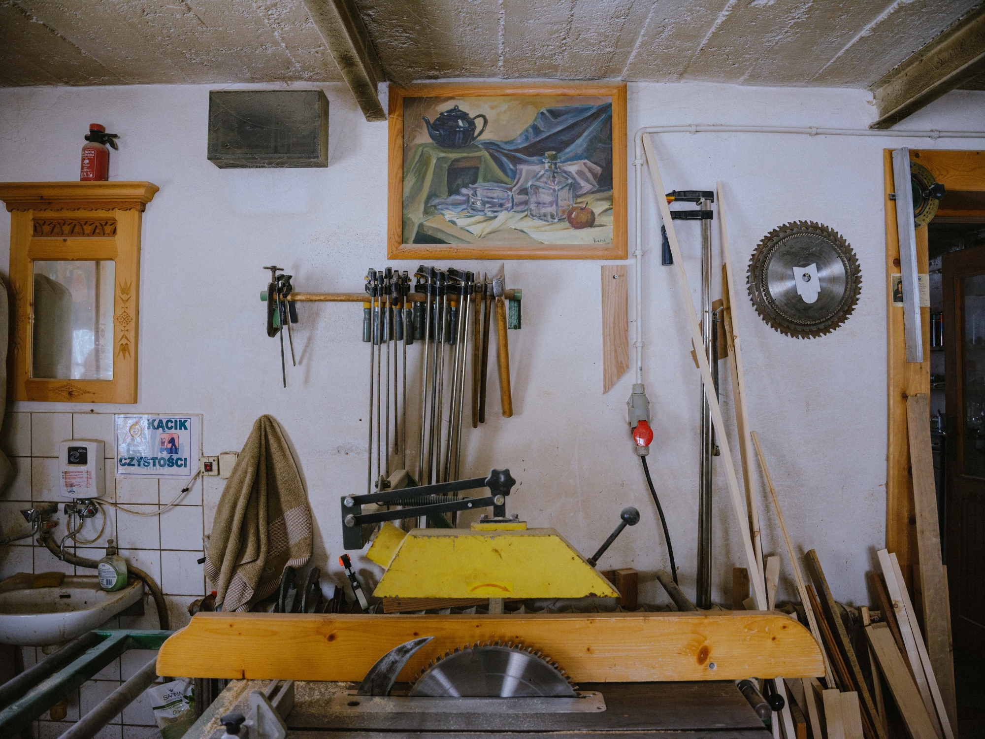 Circular saw in a craftsman’s workshop; various tools and pieces of wood around, paintings hanging on the wall