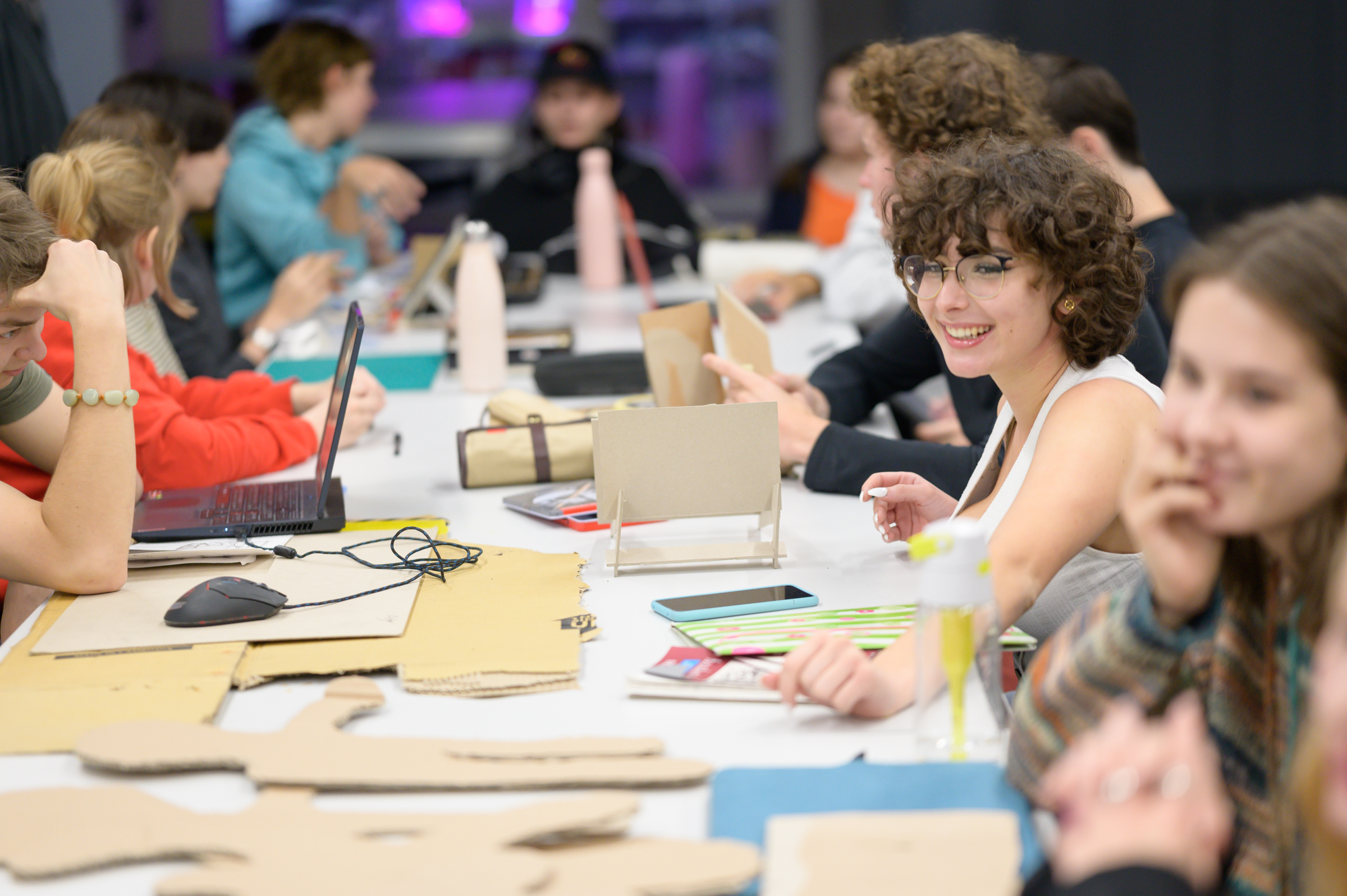 Workshop participants sitting around a large table with prototypes of their projects on it.