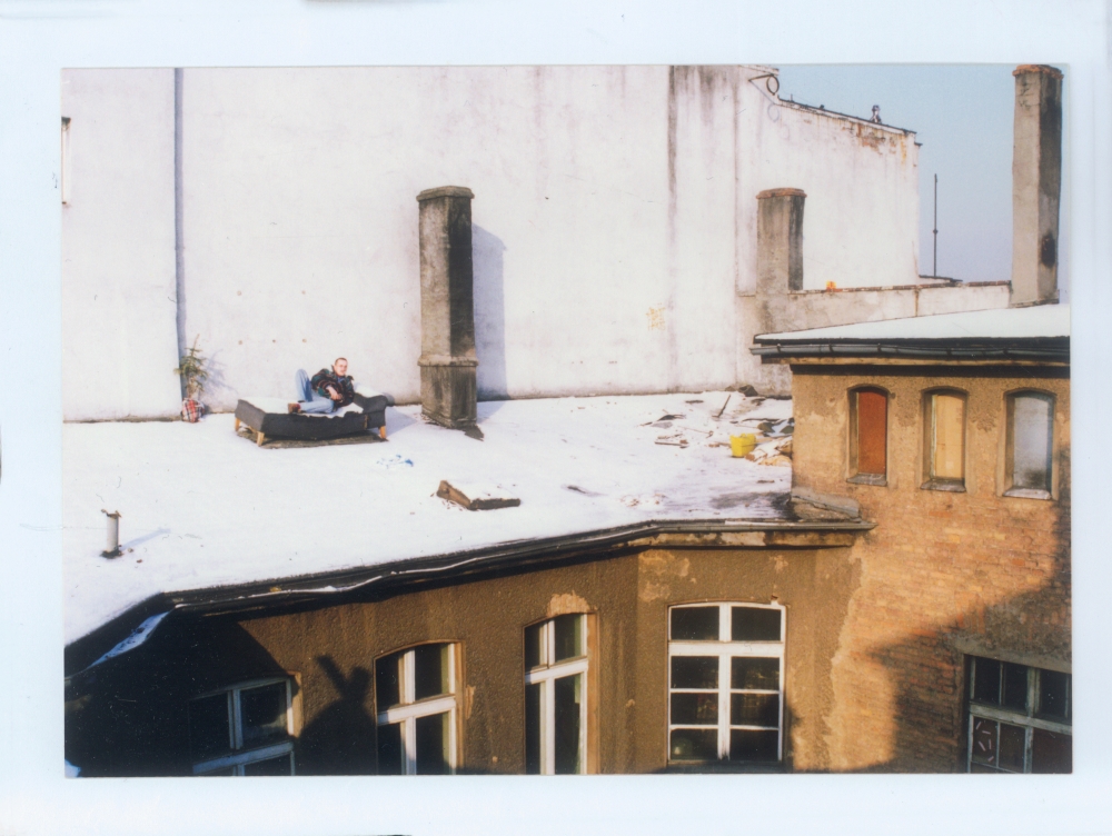 Na zaśnieżonym dachu kamienicy na kanapie leży młody mężczyzna.