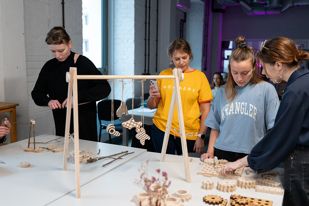 Students stand around a work table and talk about a project made of wood