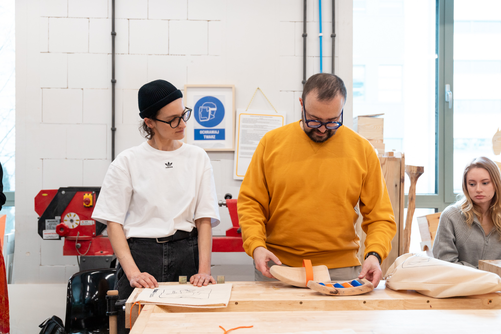 A student and a designer Jakub Szczęsny at a table looking at wood projects in a woodworking workshop