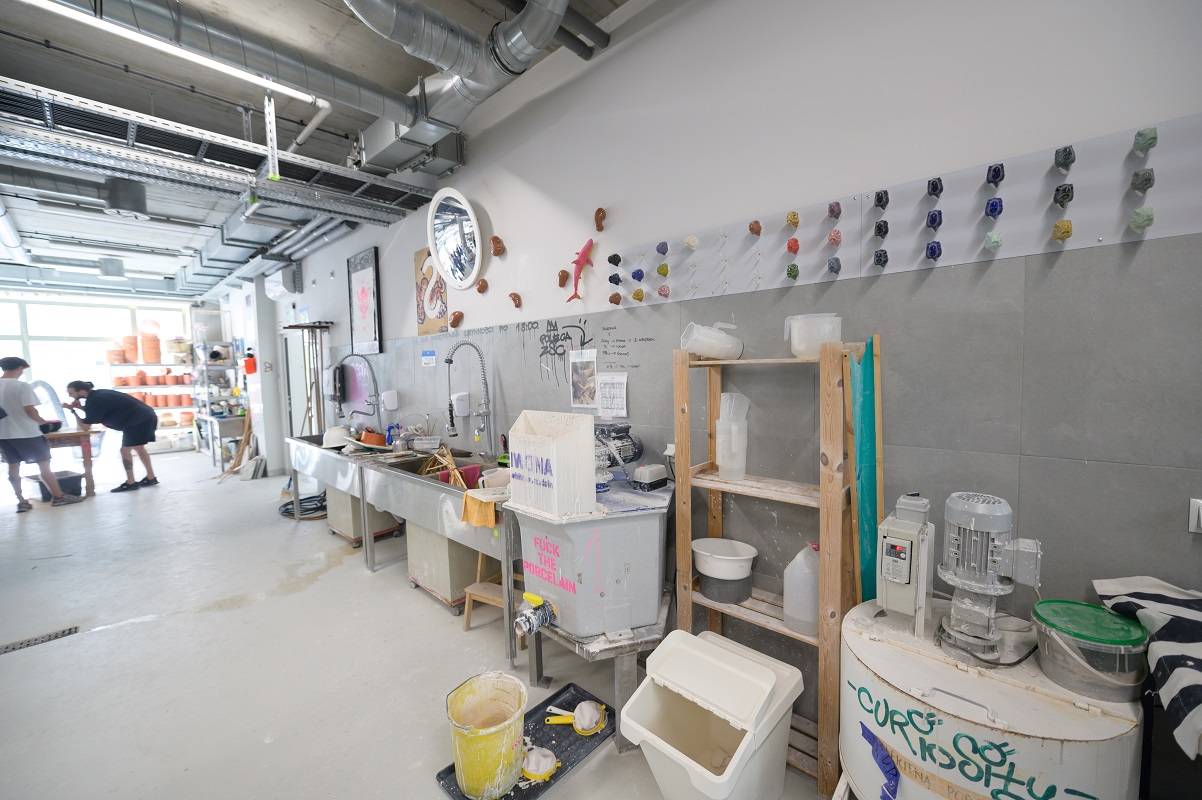 The spacious interior of the studio. Wooden bookcases and metal sinks stand against the wall.