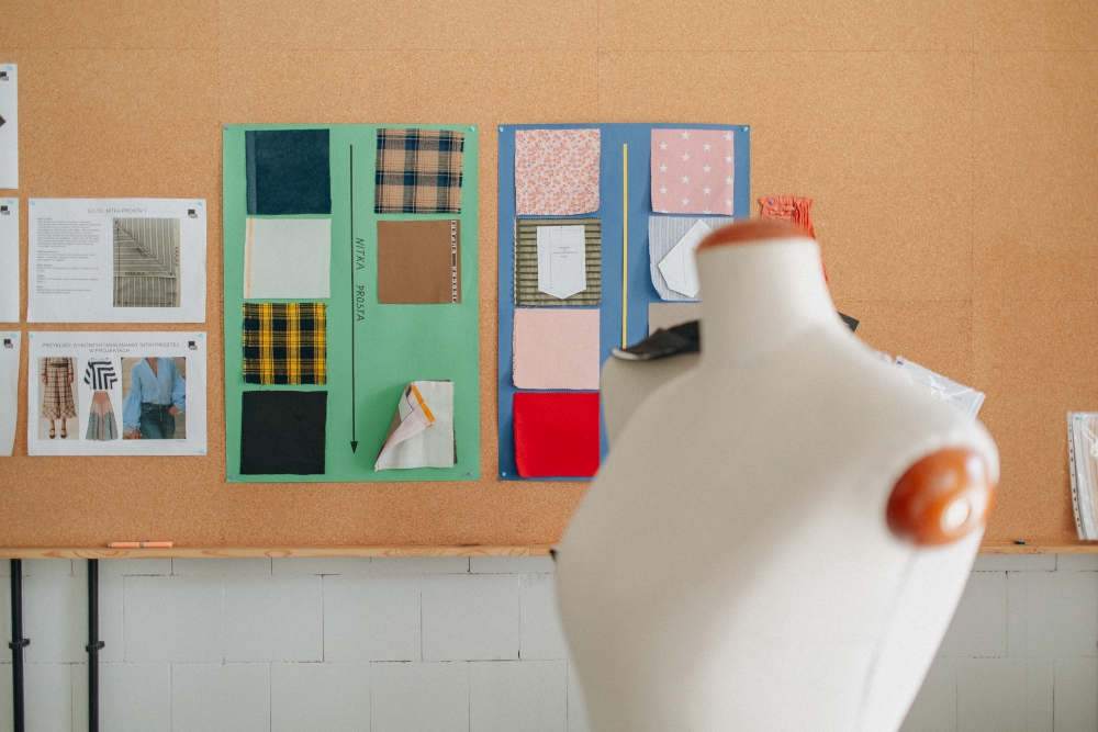 A dressmaker’s mannequin in front of a corkboard with fabric swatches pinned to it.