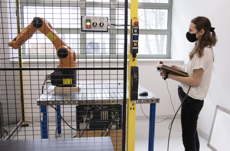 A woman operates a KUKA robot. A black net separates her from the machine for safety.