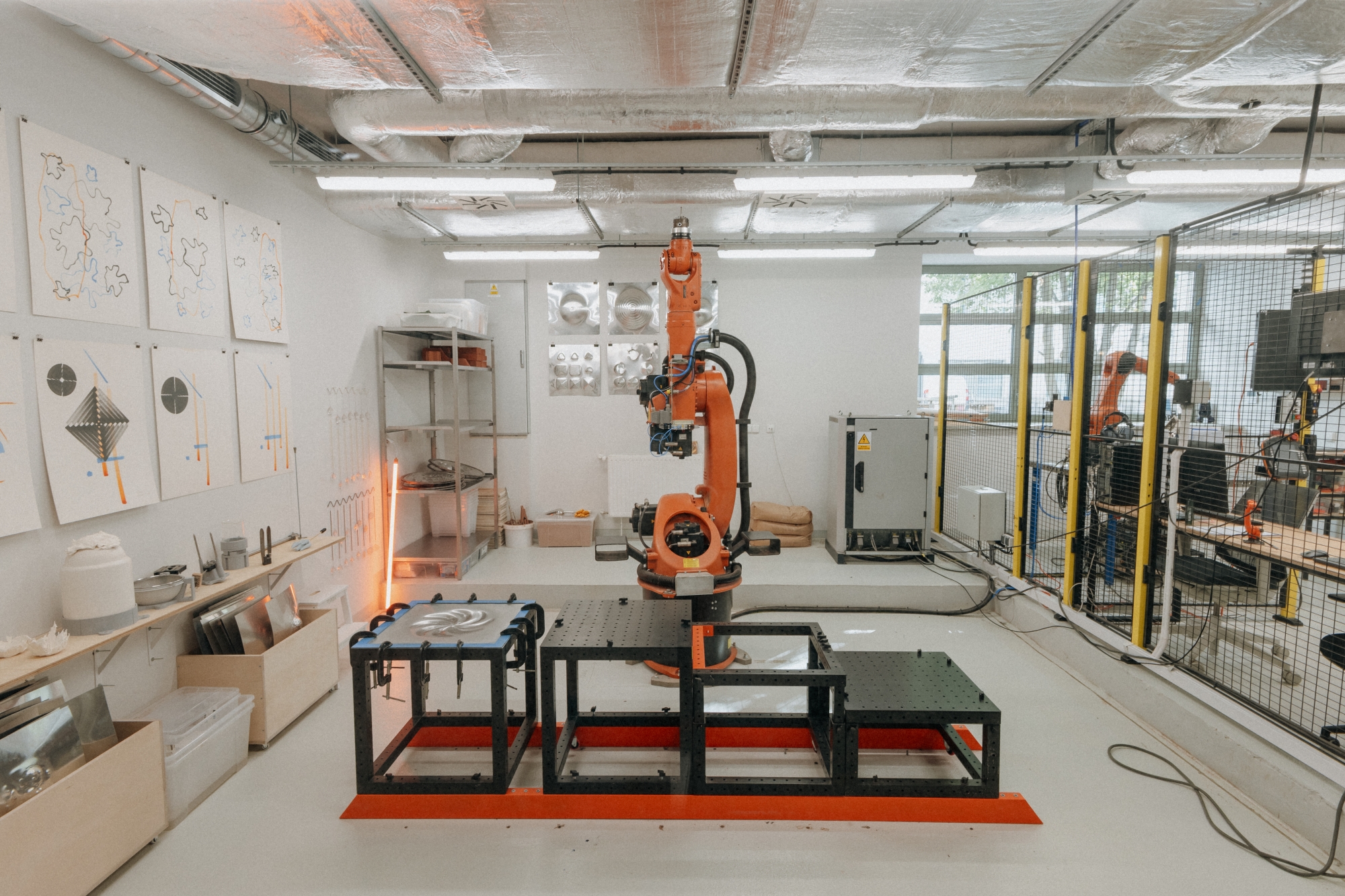 Interior of the KUKA workshop, with a large KUKA robotic arm in the center of the room.