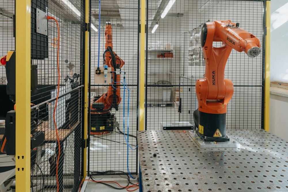 Interior of the KUKA workshop, with a KUKA robotic arm inside a fenced enclosure.