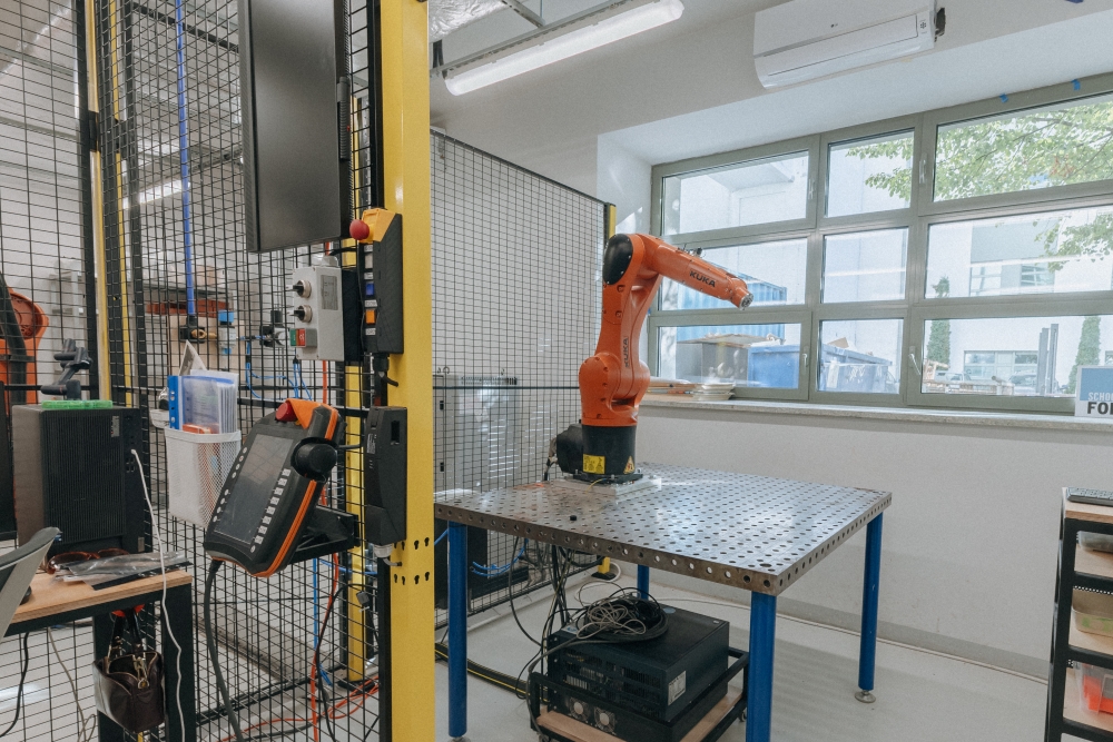 Interior of the KUKA workshop, with a small robotic arm placed on a desk.