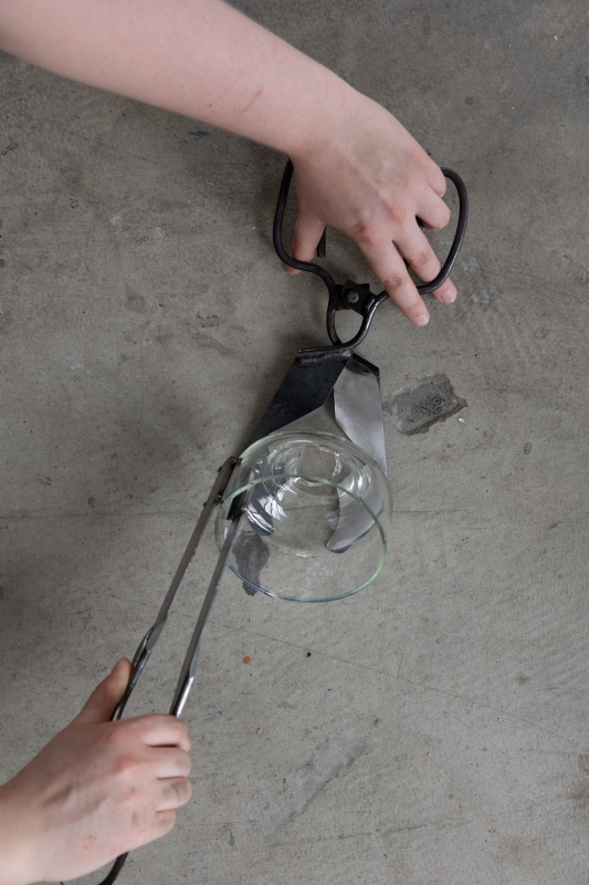 Hands using glassblowing tools to hold a glass vessel