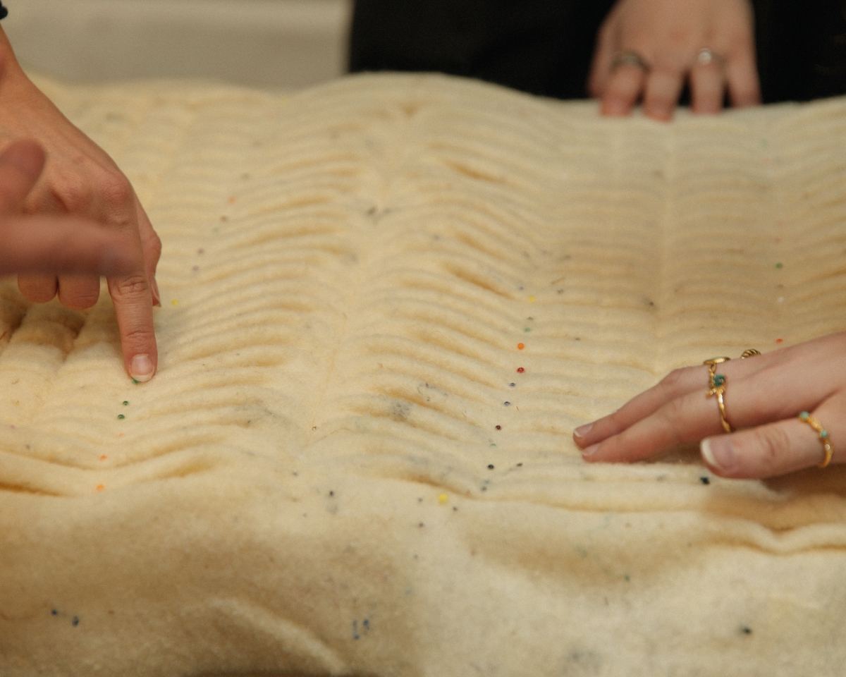 A close-up of hands touching and examining the densely pleated texture of a light-colored fabric.