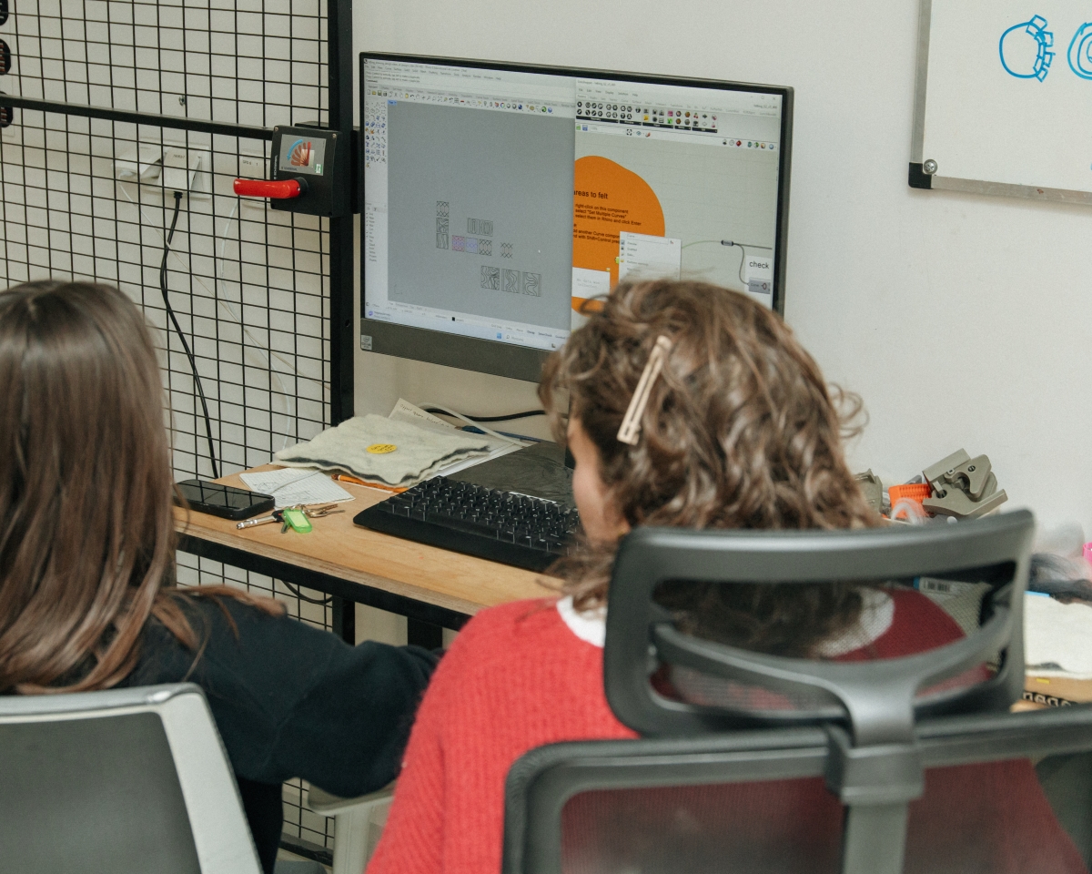 Two people sitting in front of a computer monitor showing an open 3D design program with visible diagrams and felting patterns.