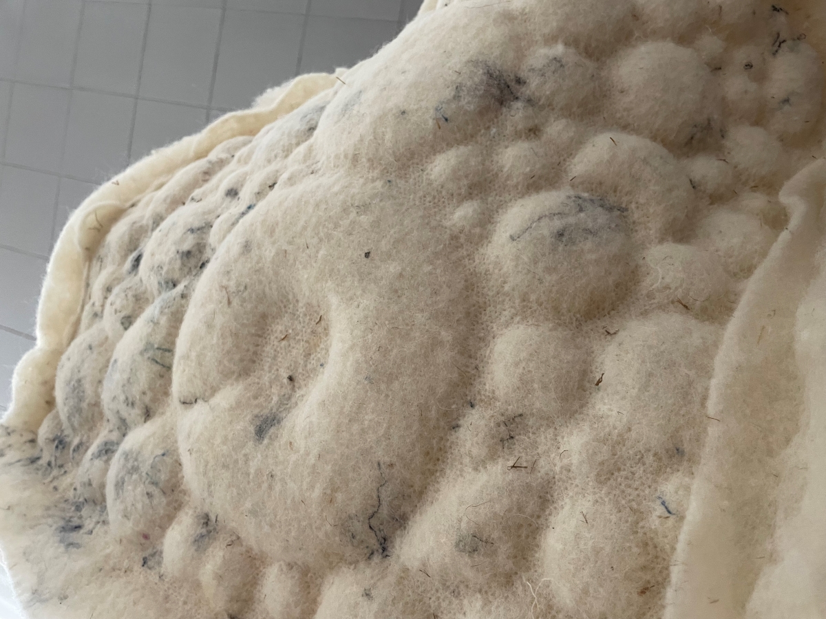 Light grey felt sample with a structural, geometric surface featuring depressions from robotic needle felting.