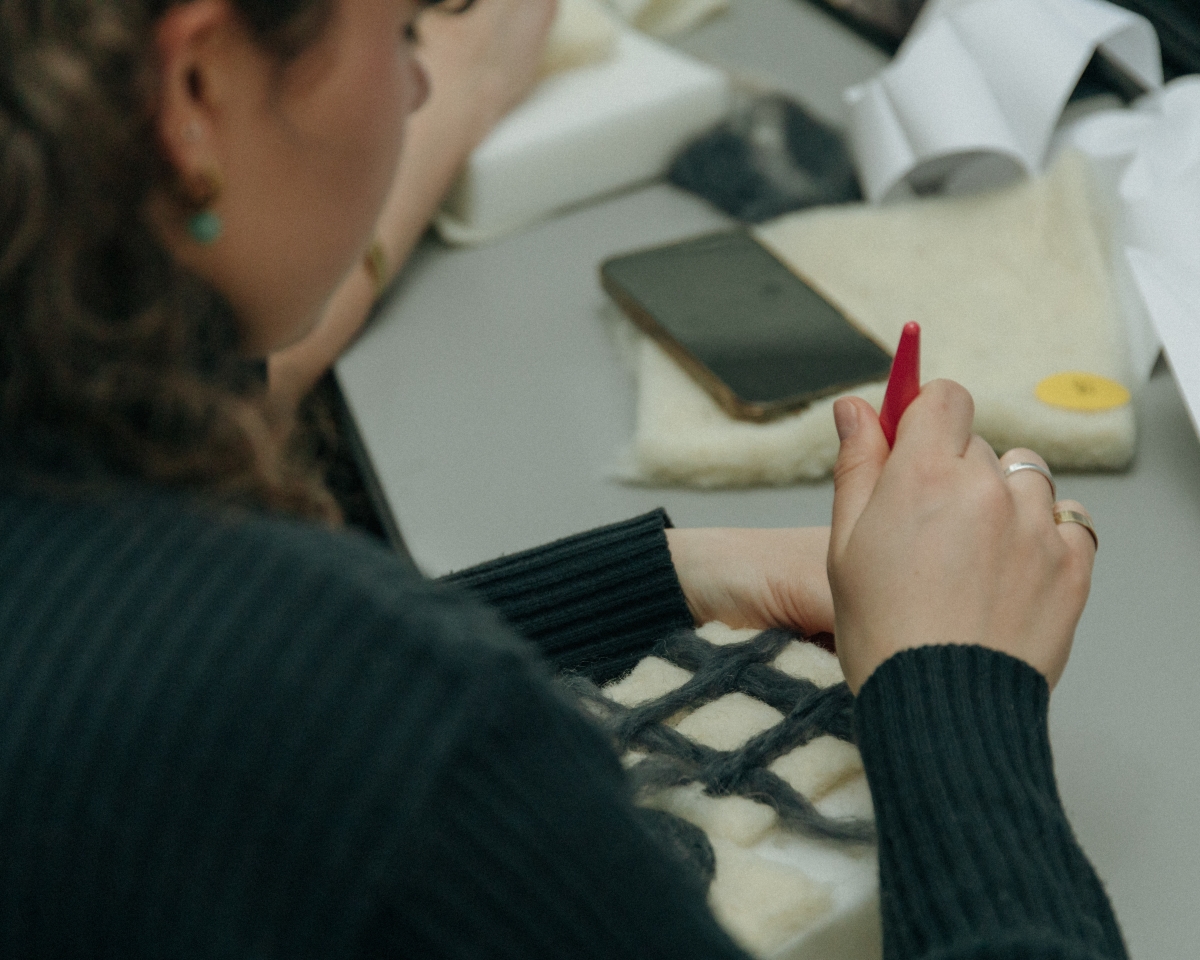 A young woman is piercing wool with a felting needle.