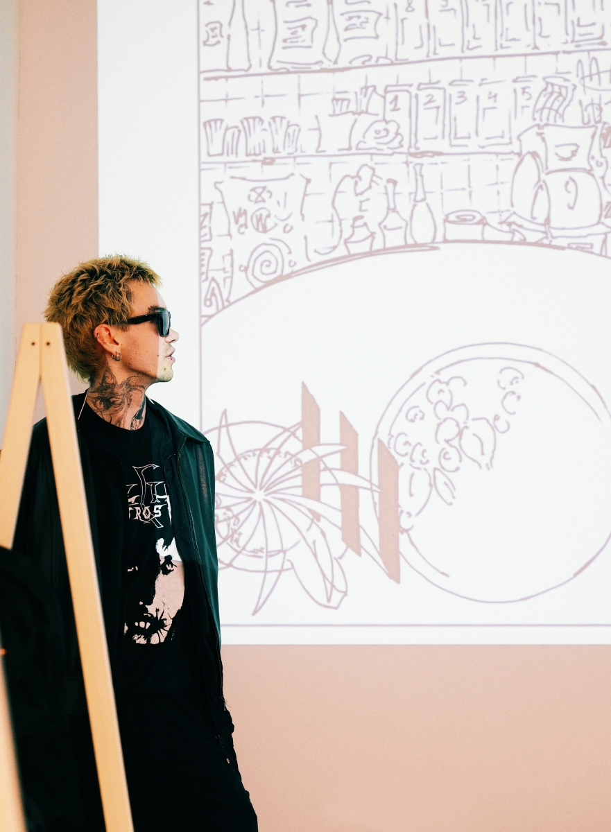 A School of Form student stands next to the screen during the presentation. The slide on display shows a sketch of a café interior.