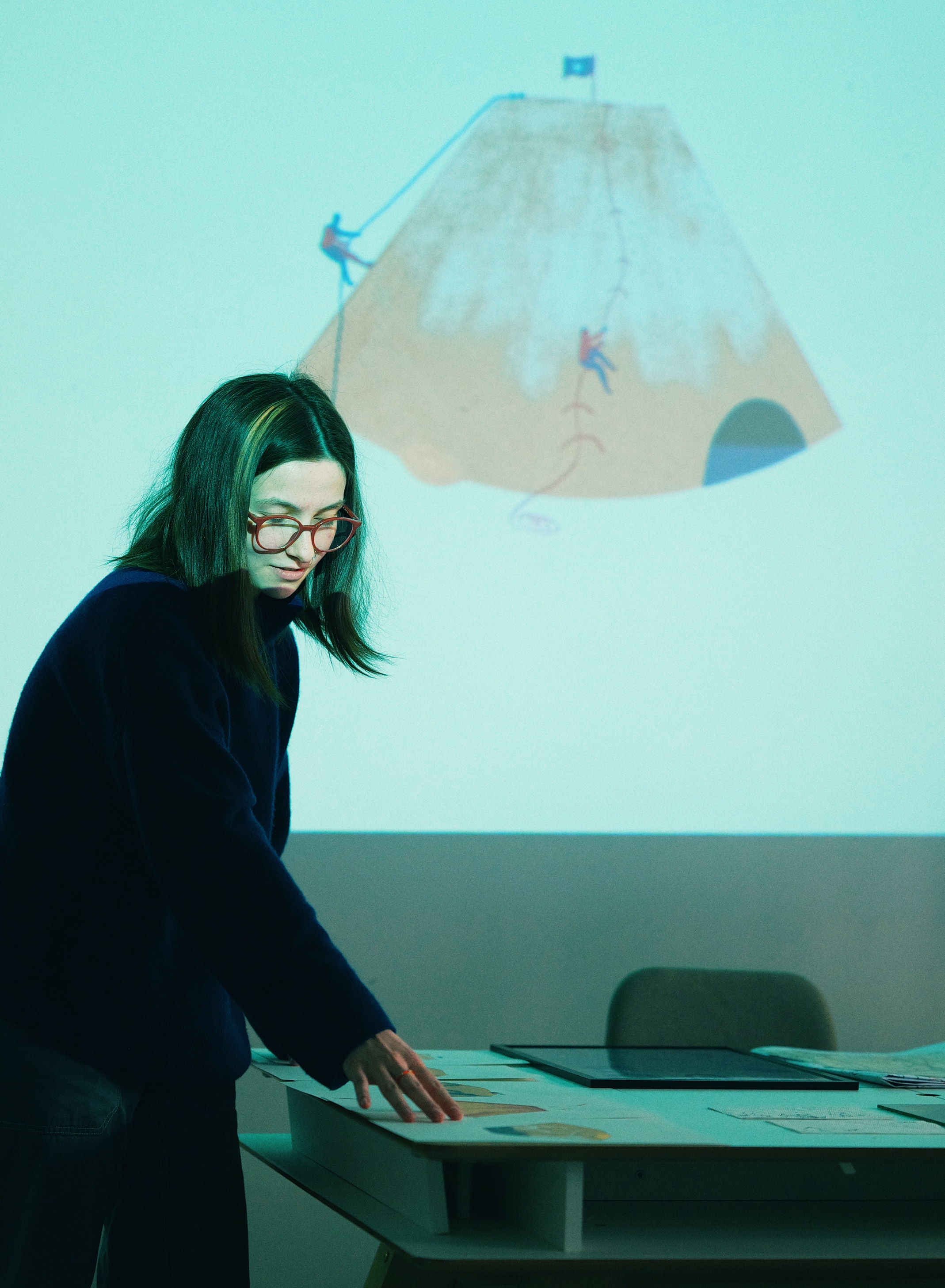 A School of Form student stands next to the screen during the presentation. The slide being displayed features an illustration of a coffee filter with mountain climbers climbing it.