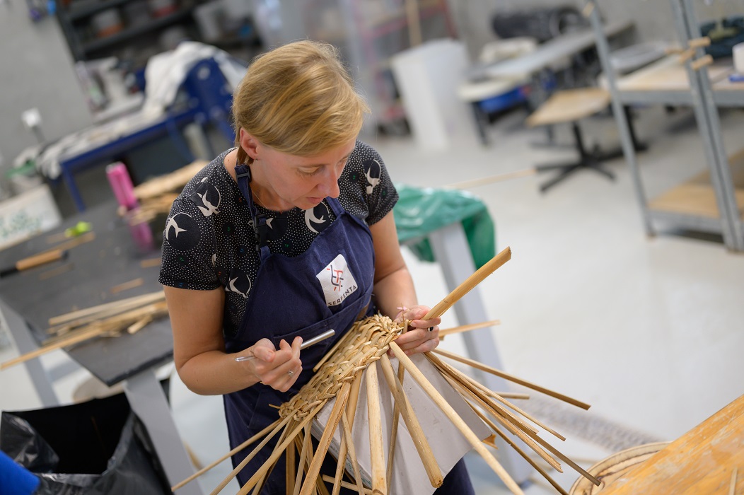 A focused woman weaves a basket out of the bulrush.