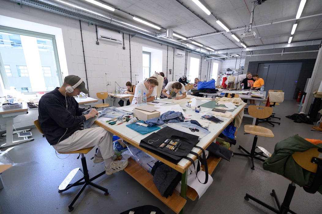 Students do sewing work at a large work table.