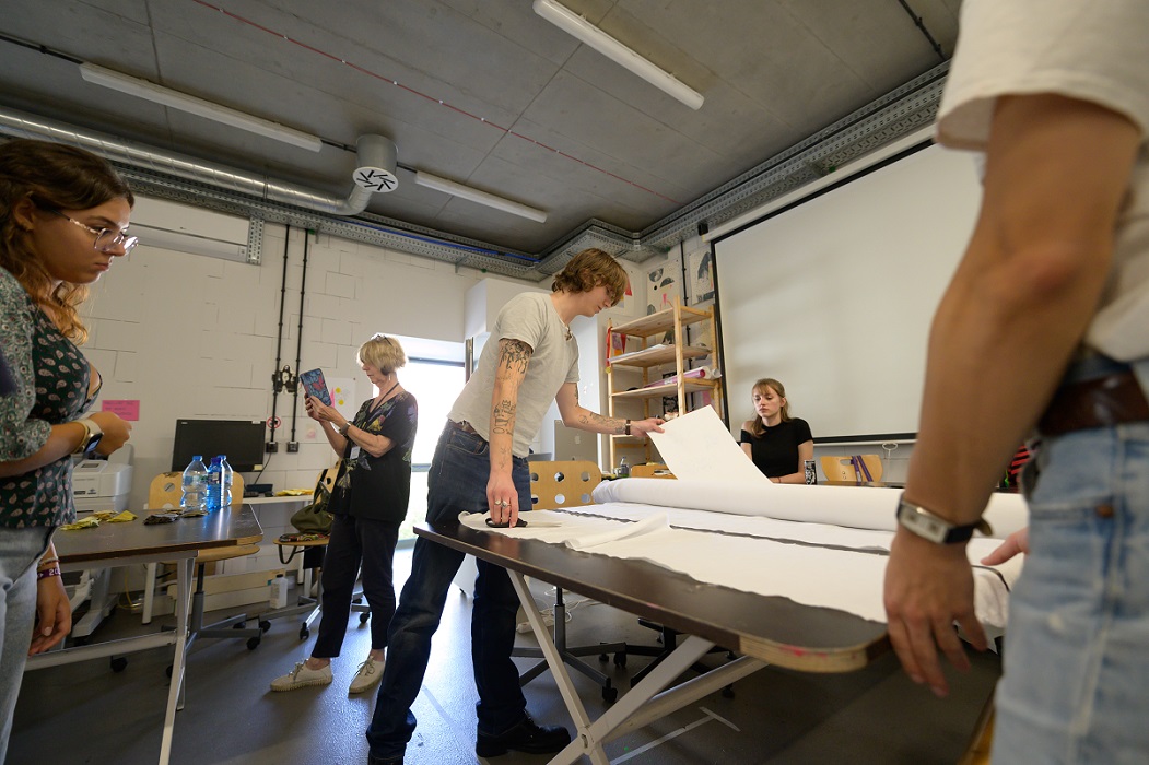 Students cut a large sheet of fabric spread out on a large sewing table.